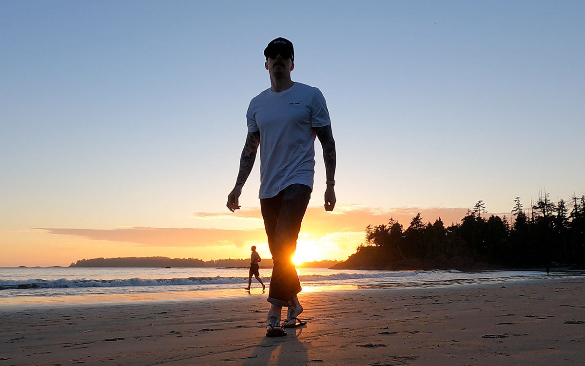 Man wearing Fault Line's Signature t-shirt walking along a beach at sunset