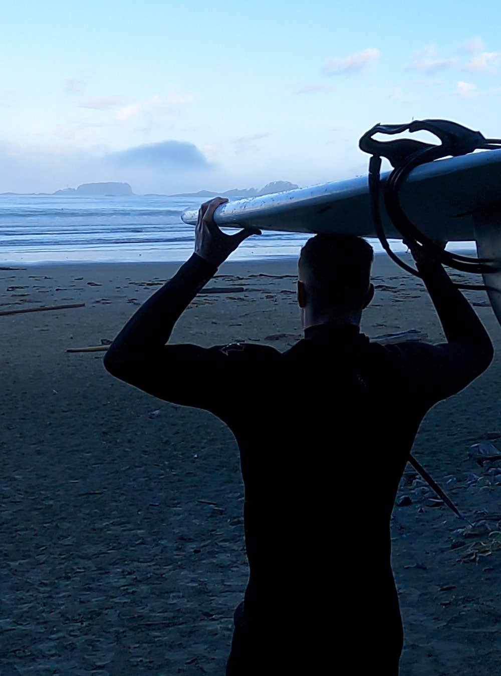 Man wearing a wetsuit carrying a surfboard on his head.