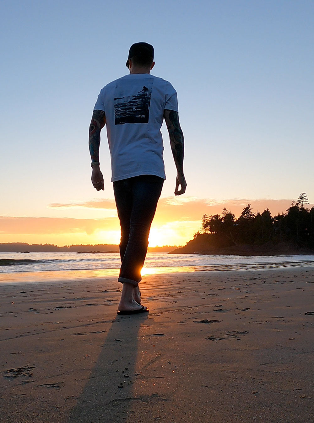 Man wearing Fault Line's Signature t-shirt walking along a beach at sunset