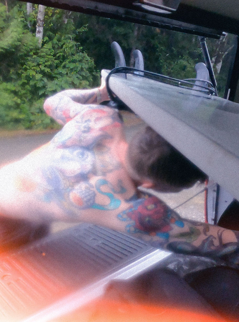 Tattooed man reaching under his surfboard in the back of his truck