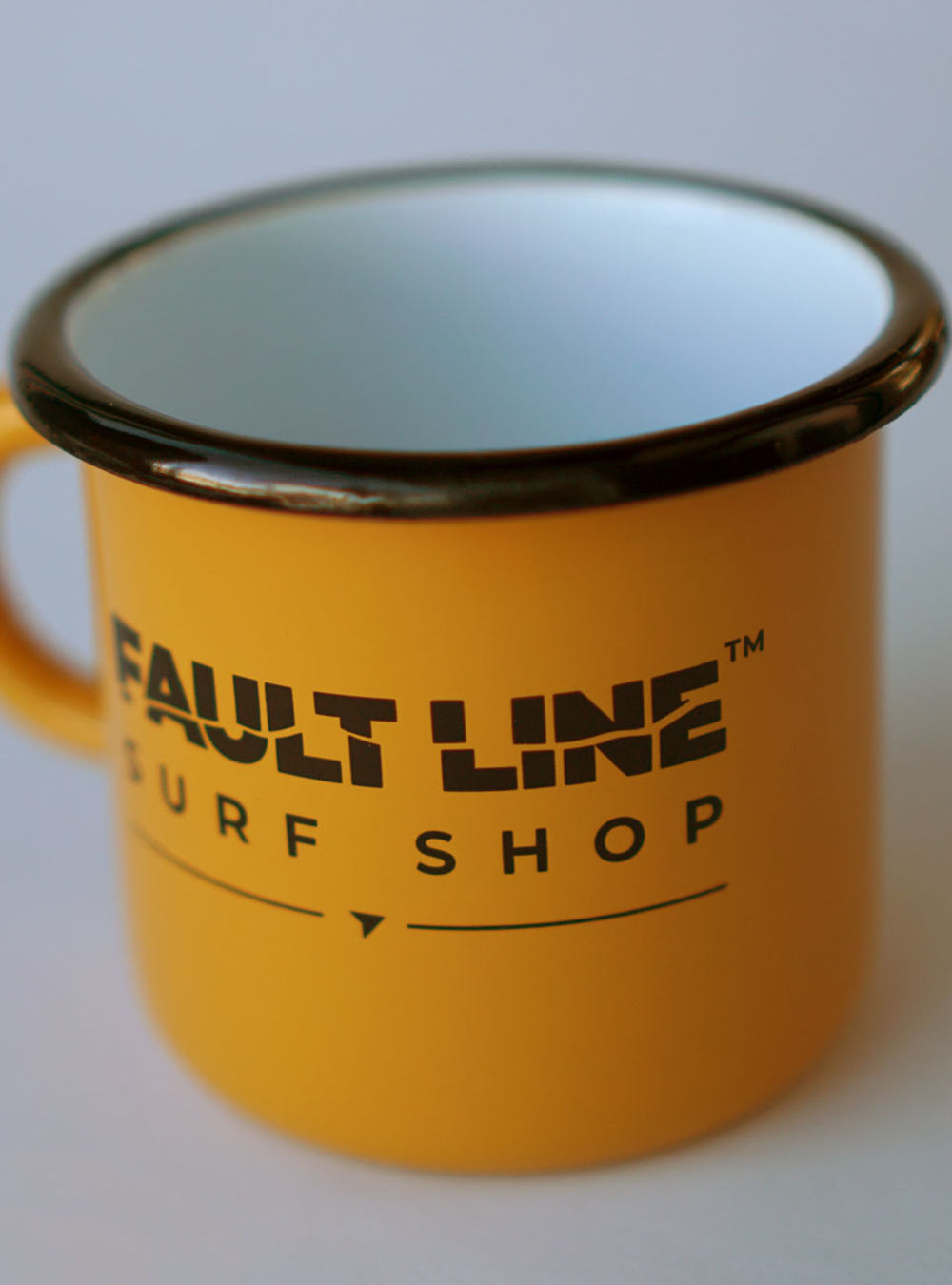 Yellow enamel camping mug with a black rim and black Fault Line logo on both sides.