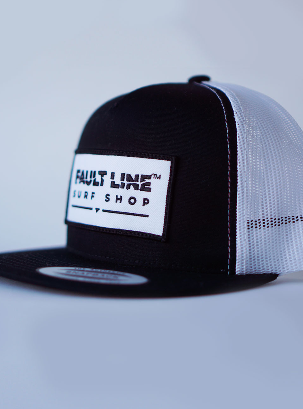 Trucker Cap with a black bill, black front and white mesh back. Fault Line embroidered Patch and black merrow-edge sewn to the front of the cap.